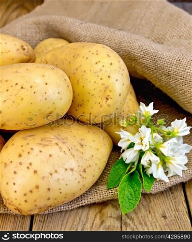 A pile of yellow potato tuber with a flower on a sacking on a wooden boards background