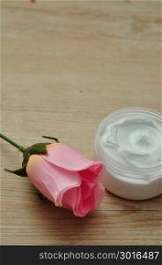 A pink artificial rose with a jar of white body lotion