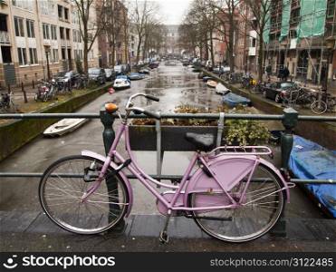 A pink bicycle locked to a railing on a bridge over a canal in Amsterdam. Bikes are a dominant form of transportation in the Netherlands.