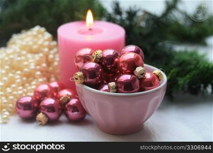 A pink candle and a bowl with small christmas balls