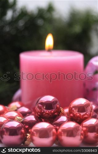 A pink candle and some small pink christmas balls