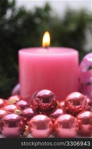 A pink candle and some small pink christmas balls