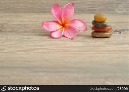 A pink frangipani flower with a pile of flat stones next to it