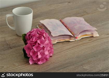A pink Hydrangea with a notebook, pencil and mug