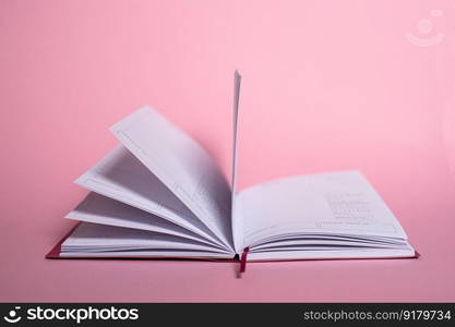 A pink notebook with a shiny decor lies next to a pen on a pink background. An open notebook for notes lies on a pink background