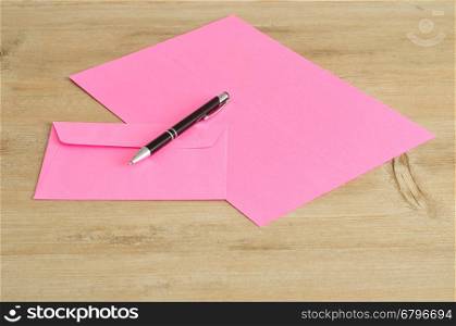 A pink paper and envelope with a pen