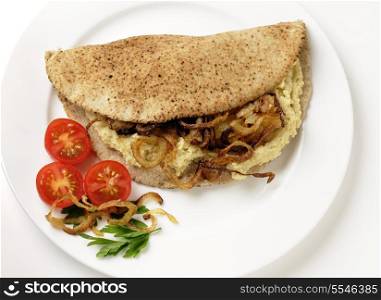 A pitta bread, or kubz, sandwich made with hummus and caramelised onions, served with a tomato and parsley garnish