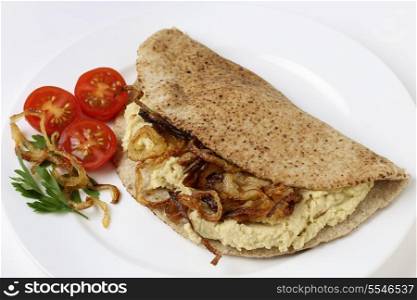 A pitta bread, or kubz, sandwich made with hummus and caramelised onions, served with a tomato and parsley garnish