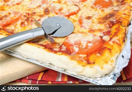 A pizze cutting wheel on a cheese and tomato Sicilian style pizza fresh from the oven