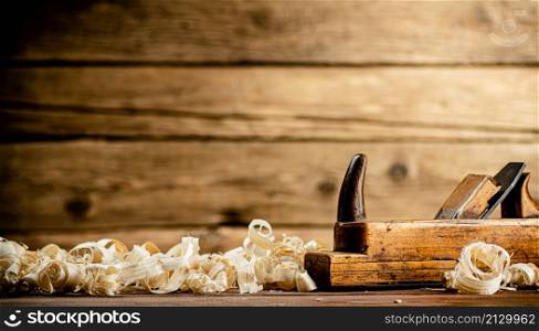 A planer with wooden shavings on the table. On a wooden background. High quality photo. A planer with wooden shavings on the table.