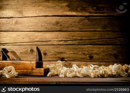 A planer with wooden shavings on the table. On a wooden background. High quality photo. A planer with wooden shavings on the table.