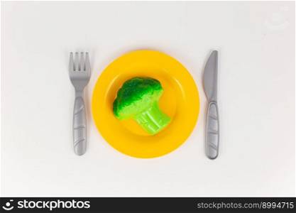 a plastic plate with a knife and fork with broccoli on a white background. plastic plate with a knife and fork with broccoli on a white background
