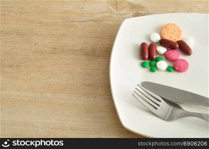 A plate filled with pills displayed with a fork and knife