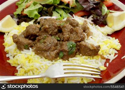 A plate of beef rogan josh, served with yellow and white rice and a salad. Rogan josh is usually made with lamb, as it is a Hindu dish, but works equally well with beef.