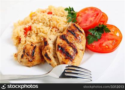 A plate of cajun chicken and rice with a sliced tomato and a fork