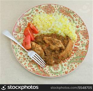 A plate of chicken and lentil curry, chicken dhansak, served with yellow and white rice and tomato seen from above