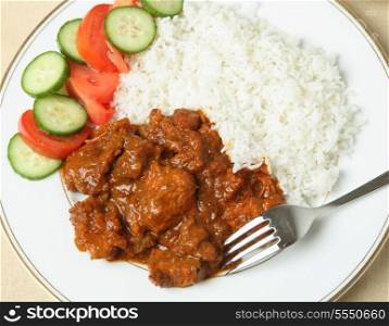 A plate of chicken tikka masala with basmati rice and a salad of cucumber and tomato.