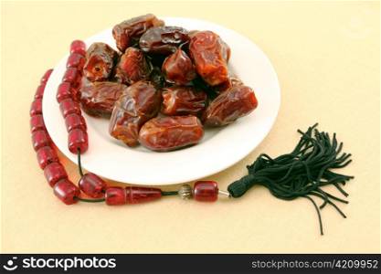 A plate of dates, eaten at fast-breaking in Ramadan, with a string of prayer beads, on a tablecloth.