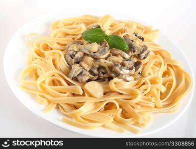 A plate of fettuccini topped with mushrooms in a cream sauce topped with a sprig of basil