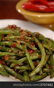 A plate of fresh-cut stir-fried green beans with a red chili sauce. There is a yellow bowl in the background.