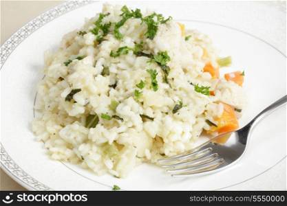 A plate of homemade chicken risotto with a fork, garnished with chopped parsley