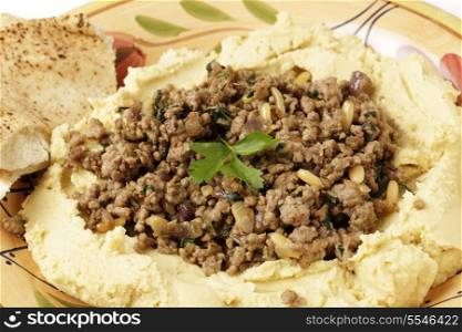 A plate of hummus chickpea dip filled with fried lamb mince, onion, pine nuts and parsley.