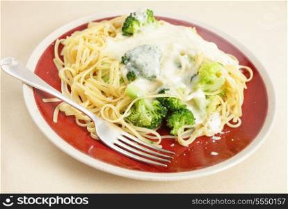 A plate of linguine pasta mixed with boiled broccoli and topped with cheese sauce and parmesan