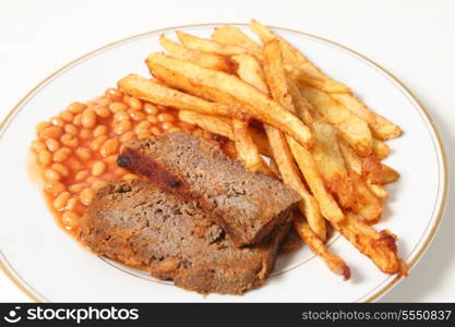 A plate of meatloaf served with baked beans and chips or french fries.