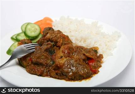 A plate of mutton vindaloo curry with rice and salad, viewed close-up
