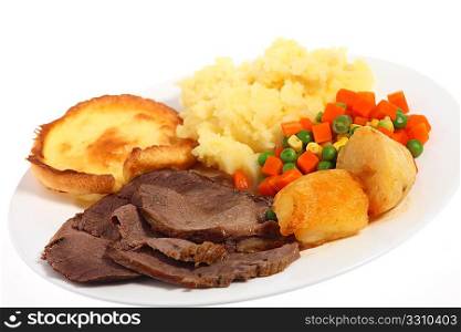 A plate of roast beef with mixed vegetables and roasted and mashed potatoes, at an angle.