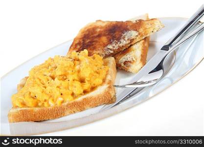 A plate of scrambled egg with black pepper on toast, with knife and fork, angled, over white