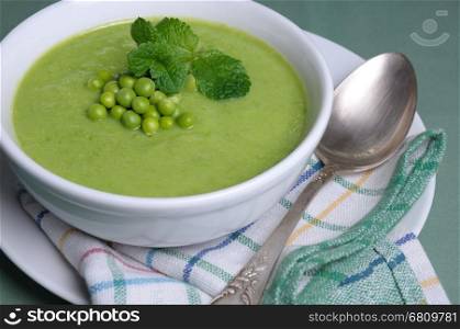 A plate of soup puree of green peas with mint on a table