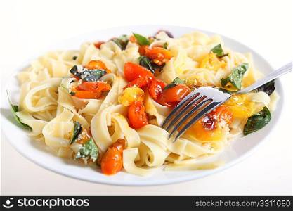 A plate of tagliatelli with roasted red and yellow cherry tomatoes tossed with oil and sprinkled with grated parmesan and a fork