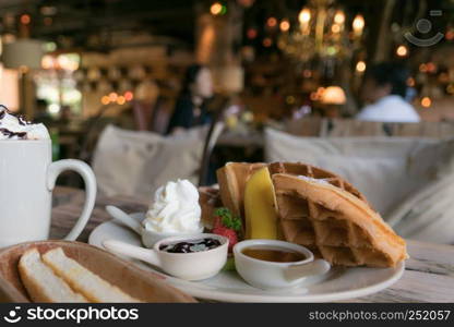 A plate of waffle with banana and strawberry, whipping cream, blueberry and syrup, delicious, yummy