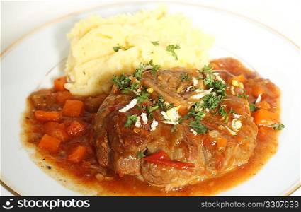A plate with an ossobuco (braised veal shank steak) in the traditional sauce, topped with gremolata (chopped parsley, garlic and lemon rind) and served with garlic potatoes.