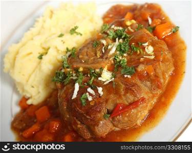 A plate with an ossobuco (braised veal shank steak) in the traditional sauce, topped with gremolata (chopped parsley, garlic and lemon rind) and served with garlic potatoes.