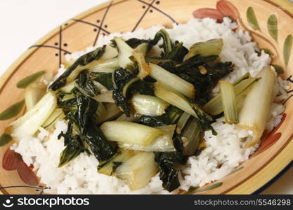 A plate with bok choi asian cabbage chopped and sauteed with sesame oil and soy sauce, served on a bed of white jasmine rice