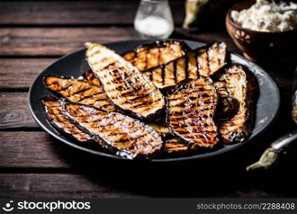 A plate with grilled pieces of eggplant. On a wooden background. High quality photo. A plate with grilled pieces of eggplant.