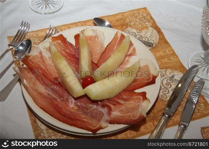 A plate with melon and parmaham, decorated with tomatoes