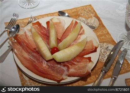 A plate with melon and parmaham, decorated with tomatoes