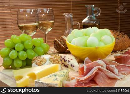 A platter of Mediterranean food including cheese, grapes, white wine, bread, Parma ham, melon, olive oil and balsamic vinegar. Shot in beautiful warm light.