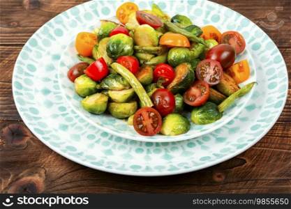 A platter of warm salad of grilled Brussels sprouts, tomato and green bush beans on a rustic wooden table.. Vegetable healthy salad with brussels sprouts.