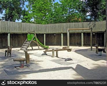 A playground in the middle of a forest, in a fort with sand on the ground.