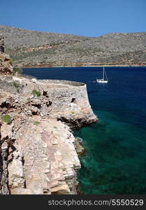 A pleasure yacht sails past the fortifications on the northern, seaward, side of the Venetian fortress and former leper colony of Spinalonga, in Crete, Greece.