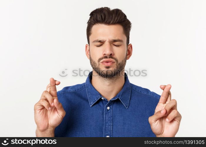 A portrair of a young man with crossed fingers and closed eyes praying for risky business. A portrair of a young man with crossed fingers and closed eyes praying for risky business.