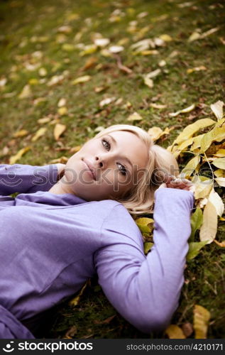 A portrait of a beautiful caucasian woman lying down on autumn leaves on the ground