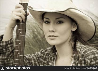 A portrait of a beautiful cowgirl with a guitar in sepia tone