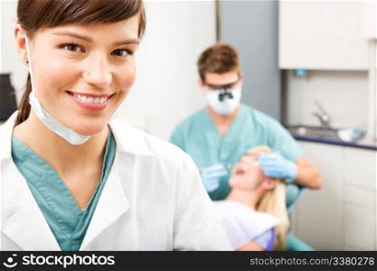 A portrait of a dental assistant smiling at the camera with the dentist working in the background