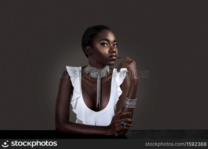 A portrait of a flirtatious young black female with short black hair, moist lips, perfectly manicured nails wearing a white sleeveless blouse with silver jewelry sitting at the bar.