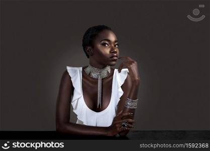 A portrait of a flirtatious young black female with short black hair, moist lips, perfectly manicured nails wearing a white sleeveless blouse with silver jewelry sitting at the bar.